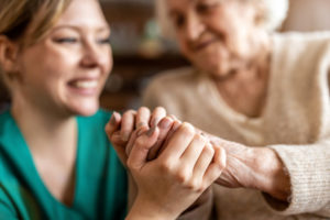 A smiling healthcare worker is clasping the hand of a smiling senior woman.